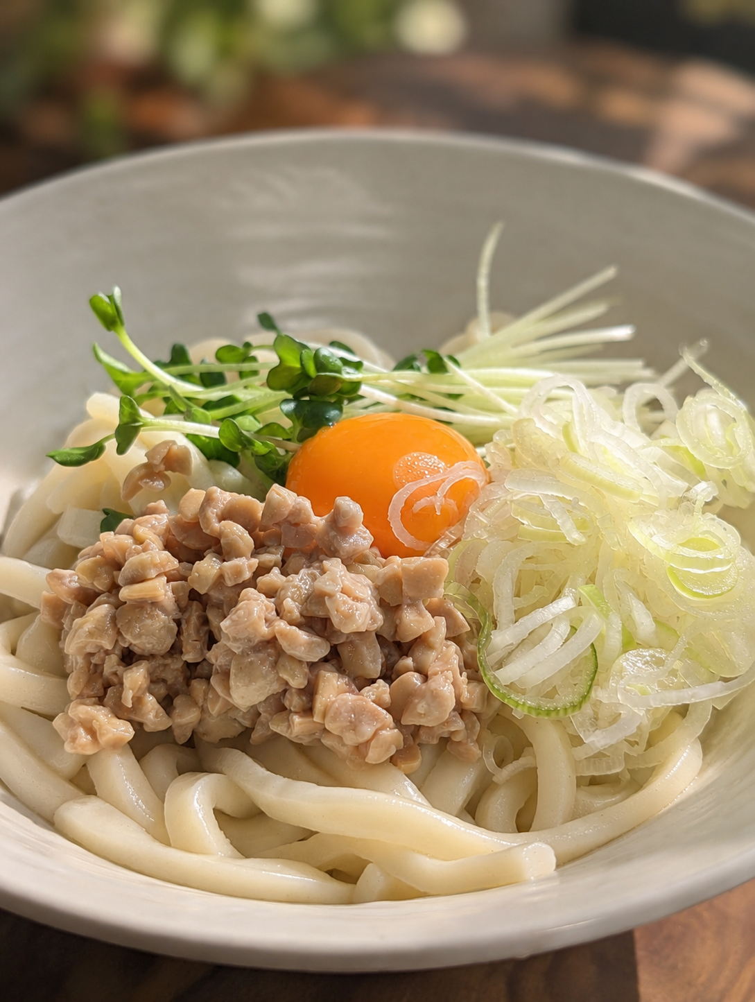 納豆と卵が乗った白い器のうどん